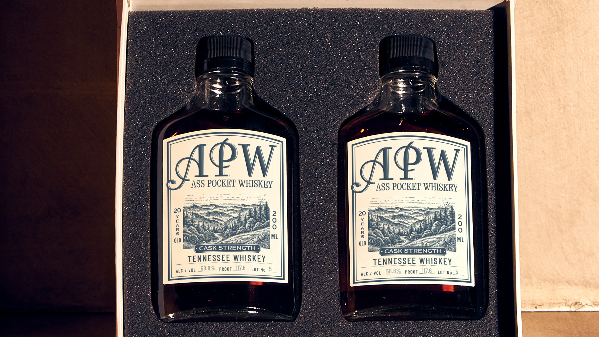 Two bottles of A.P.W. Tennessee Whiskey in a box on a wooden surface.